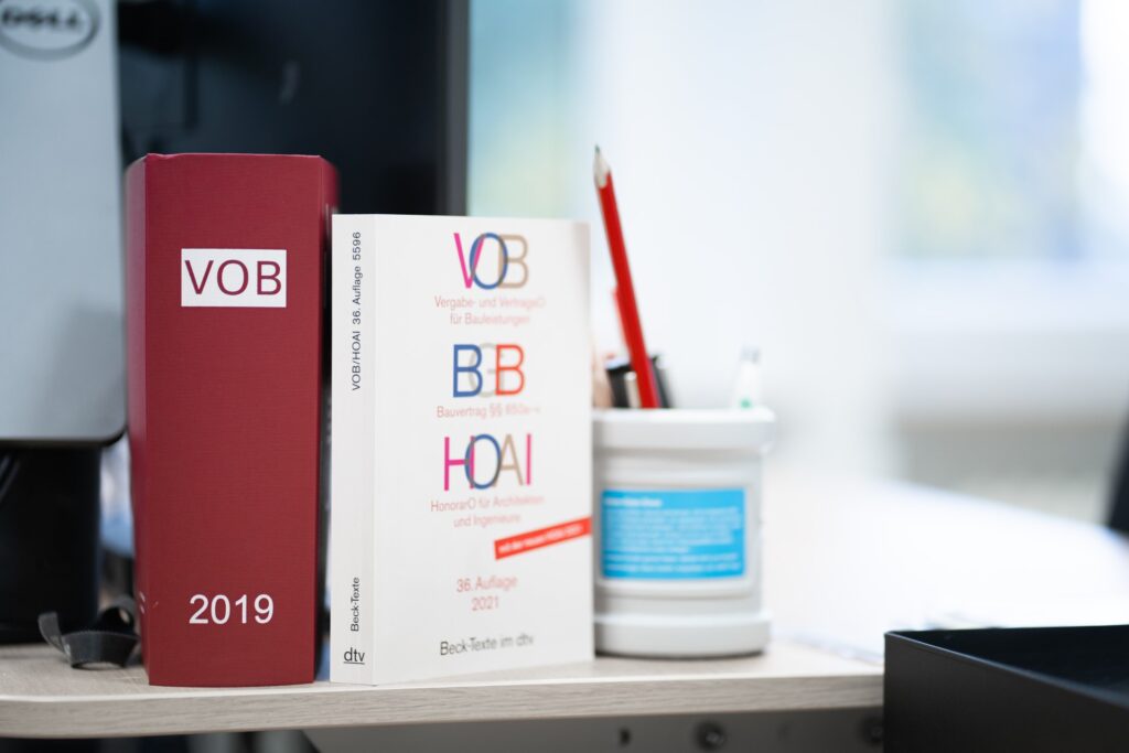 Bücher zu VOB und HOAI stehen neben einem Stiftebecher auf einem Schreibtisch
