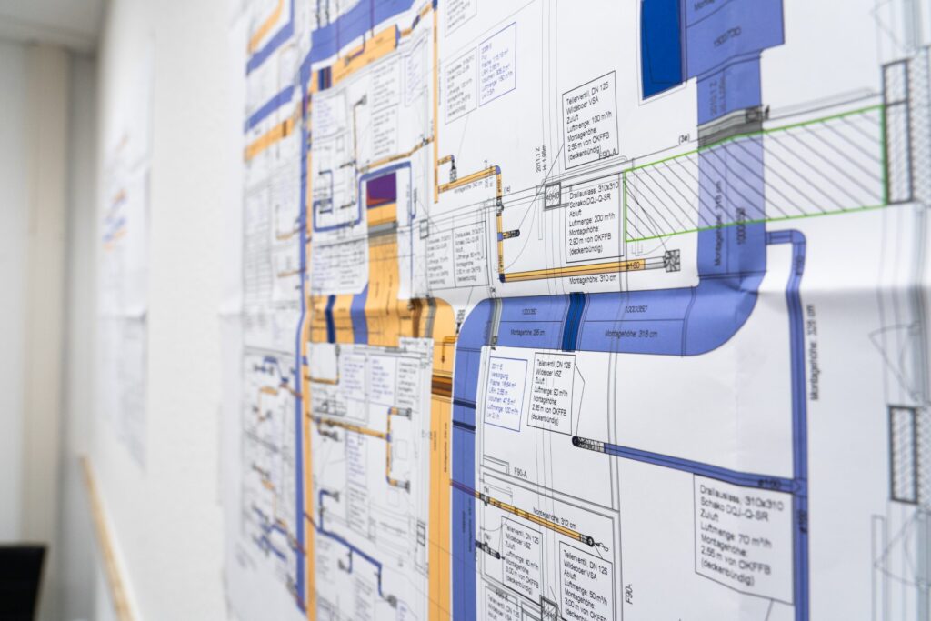 Technische Bau- und Installationspläne mit farbigen Leitungswegen an einer Wand prüfen