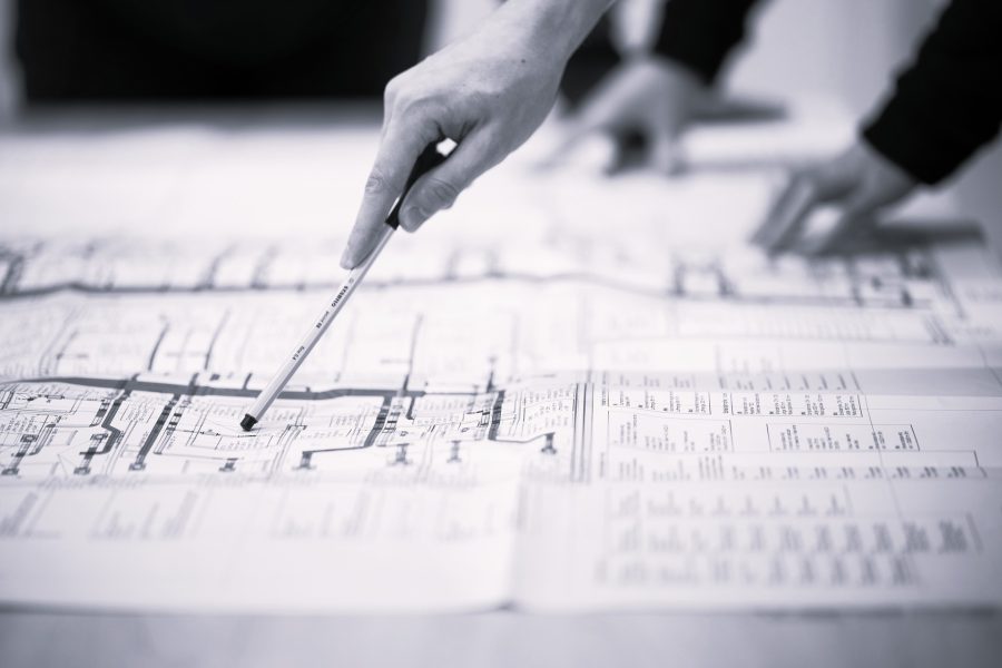 Hand mit Stift über Bauplänen bei einer Planungsbesprechung